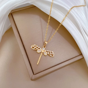 Close-up of a gold-plated dragonfly necklace with sparkling crystals on silk fabric