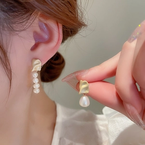 Detail of asymmetrical gold earrings featuring clusters of pearls and matte metallic texture