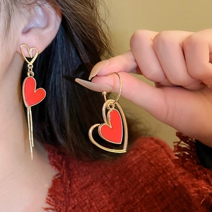 Detail of red hollow heart earrings with asymmetric gold tassel hanging from ear