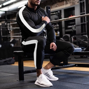 Detail of slim-fit men's black tracksuit featuring white side stripes in gym setting