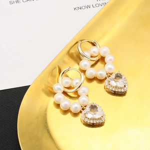 Detail of heart-shaped zircon pendant and round natural pearl earrings in golden finish