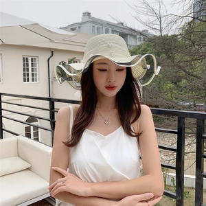 Detail of light beige straw sun hat with pearl accents and wavy striped large brim