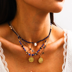 Detail showing layered gold-plated necklaces with sun pendant and natural pearl accents