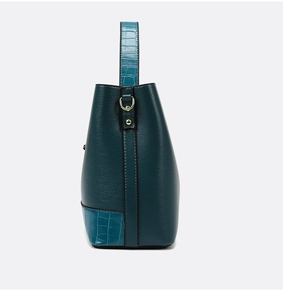 Detail of dark teal bucket bag featuring pebble grain leather and crocodile texture accents