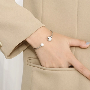 Silver flower bangle with pearl accent shown on wrist over a beige blazer sleeve