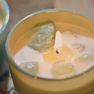 Scented crystal candle in yellow jar with green raw stones and bright burning flame