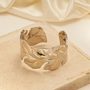 Detail of gold leaf texture cuff bracelet resting on beige stone with silk background