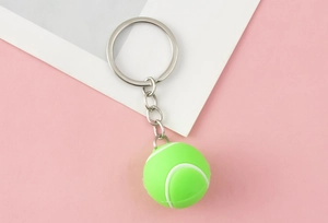 Detailed view of 3D neon green tennis ball keychain with silver metal ring on pink background