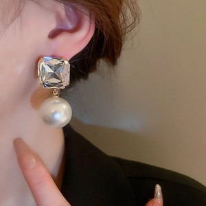Close-up of elegant square crystal and pearl drop earrings worn by a model