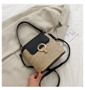 Close-up of woven straw bucket bag featuring a black leather flap and round gold metal lock