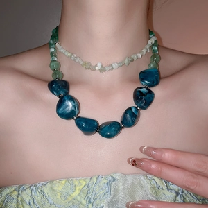 Detail of layered acrylic necklace featuring irregular blue resin beads and green accents
