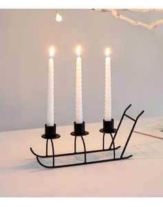 Elegant black metal sled candle holder with three lit white spiral candles for Christmas