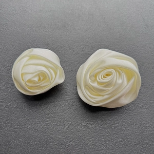 Close-up of two handmade cream satin rose buds with layered fabric petals and silk luster