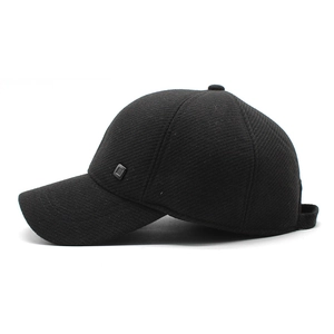 Detail of winter baseball cap with earflaps and gray metal badge on black fabric