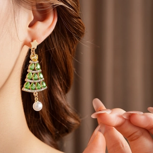 Close-up of golden Christmas tree earring with green crystals and a dangling pearl