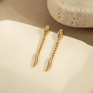 Close-up of gold snake earrings with sparkling crystals on a textured ceramic surface