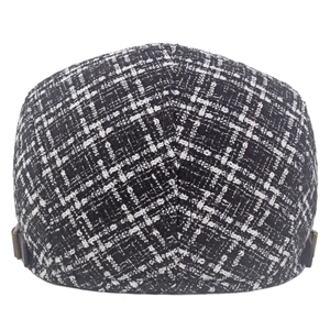 Dettaglio del berretto newsboy in tweed bianco e nero con fibbie metalliche laterali