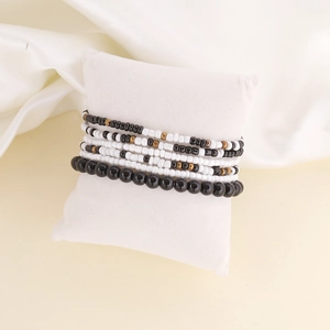 Macro shot of multi-layer white and black beaded bracelet set on a white soft velvet cushion
