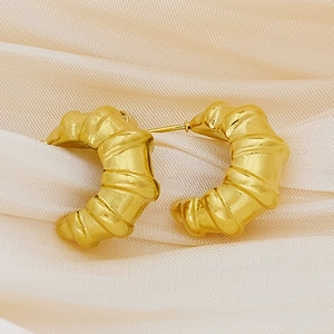 Detail of gold-plated croissant earrings with matte pleated texture on silk background
