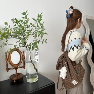 Detail of plaid canvas backpack with plush lamb charm and side brand label display