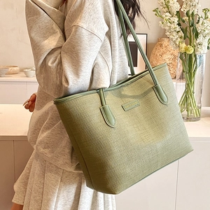 Minimalist green woven tote bag with metallic logo plate shown on a shoulder