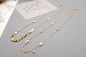 Detail of gold-plated chains with baroque freshwater pearls and heart charms on gray surface