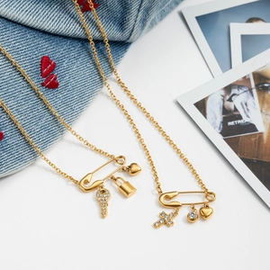 Detail of gold paperclip necklaces with heart, key and cross charms on denim background