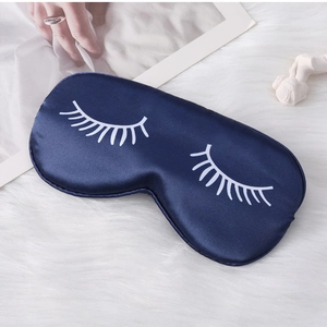 Detail of dark blue satin sleep mask with white eyelash print on soft plush background