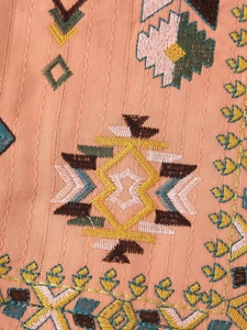 Macro shot of ethnic geometric embroidery on coral orange textured fabric vest
