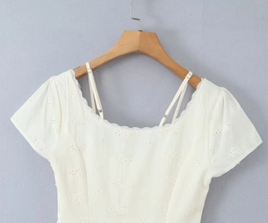 Detailed view of white short-sleeve lace dress with intricate hollow embroidery and straps