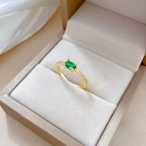Macro shot of oval green zircon ring with gold band and diamonds in a beige jewelry box
