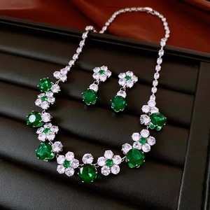 Close-up of silver flower jewelry set with green crystals on dark velvet tray