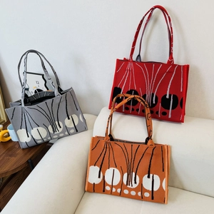 Close-up of three knitted tote bags in grey, red, and orange with abstract plant patterns