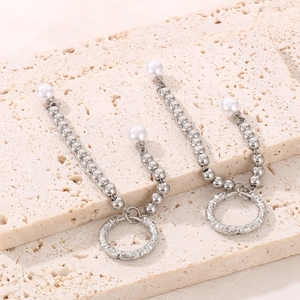 Close-up of long silver chain earrings with white pearls on a textured stone surface
