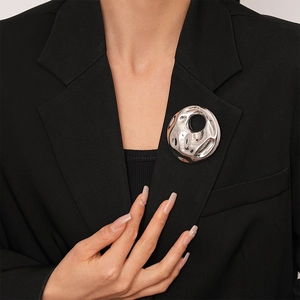 Close-up of a silver irregular crumpled metal brooch on a black suit blazer