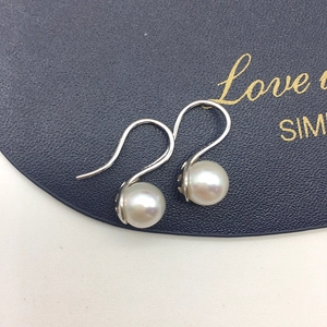 Detailed view of round white freshwater pearls with silver hooks on dark textured background