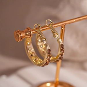 Close-up of gold geometric hoop earrings with amber rhinestones on a display stand