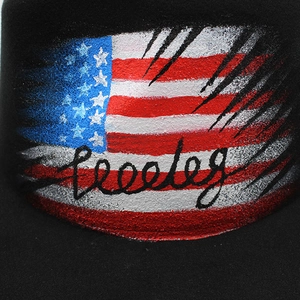 Macro detail of hand-painted American flag print on a black fedora hat with artistic text