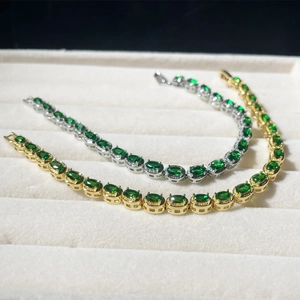Detail of gold and silver tennis bracelets with oval green emeralds on white velvet