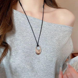 Détail d'un pendentif ovale argenté sur cordon noir porté par un mannequin élégant