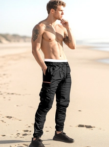 Close-up of black cargo pants featuring side flap pockets and elastic cuffs on a beach