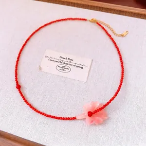 Red beaded necklace with a pink flower pendant and gold-tone chain on white linen