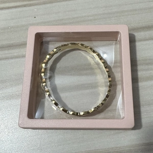 Golden textured bracelet in a pink PE film floating display box on a wooden desk