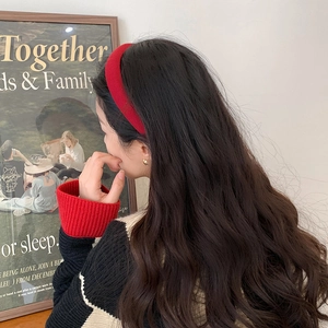 Detailed view of a red knitted headband on a model with long wavy dark brown hair