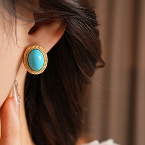 Close-up of a vintage gold earring with a round turquoise stone on a female model