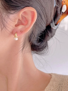 Close-up of elegant gold hoop earrings with white round pearls on a female model