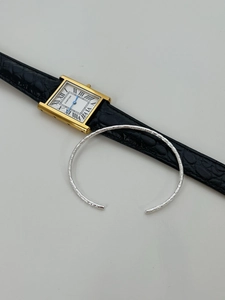Vue détaillée du bracelet jonc argenté texturé porté avec une montre classique