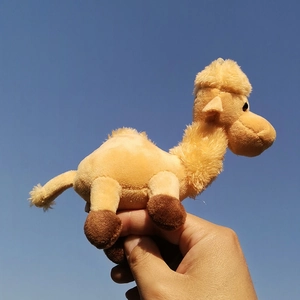 A small brown camel plush keychain being held by a hand against a clear blue sky background