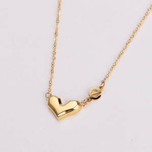 Detailed macro view of a gold geometric heart pendant and letter e on a delicate chain