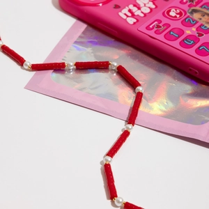Detail of red beaded phone charm strap with pearls and gold accents on white surface